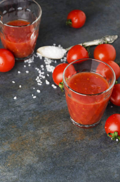 Вид зверху на томатний сік, свіжі вишневі помідори та сіль на темному кухонному столі
 - Фото, зображення