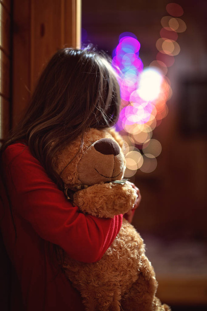 little girl hugs a teddy bear in the evening at home - 写真・画像