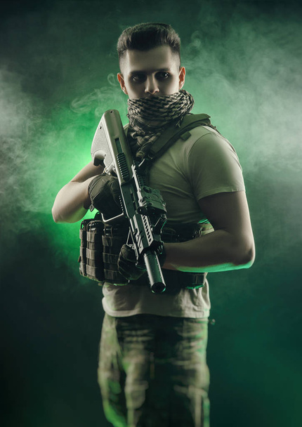 mens in militaire speciale kleren poseren met een pistool in zijn handen op een donkere achtergrond in de nevel - Foto, afbeelding