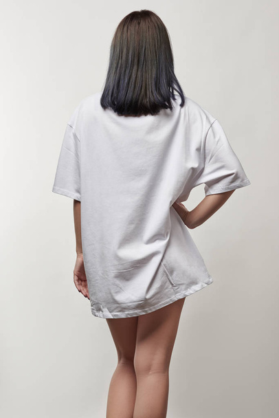 задний вид молодой женщины в белой крупногабаритной футболке с копировальным пространством, изолированным на сером
 - Фото, изображение