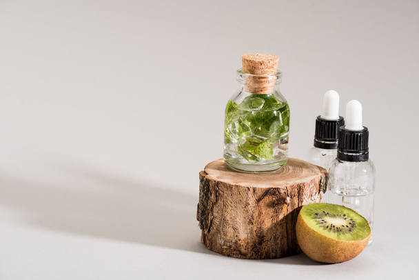 Studio shot of glass bottle with mint, kiwi and serum bottles on grey - Photo, Image