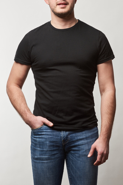 partial view of man with hand in pocket in denim and black t-shirt with copy space isolated on grey  - Photo, Image