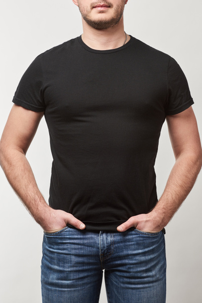 vista parcial del hombre con las manos en bolsillos en camiseta negra con espacio de copia aislado en gris
  - Foto, Imagen