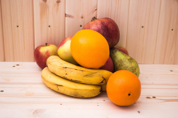 Varias frutas manzanas, plátanos, naranjas, granadas sobre fondo de madera natural. Alimento saludable
 - Foto, imagen