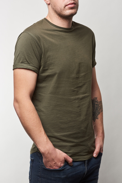 cropped view of tattooed man in khaki t-shirt with copy space isolated on grey - 写真・画像