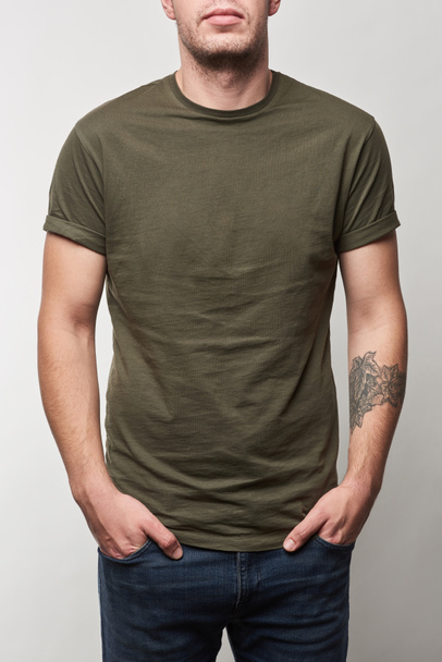 partial view of tattooed man in khaki t-shirt with copy space isolated on grey - Foto, afbeelding