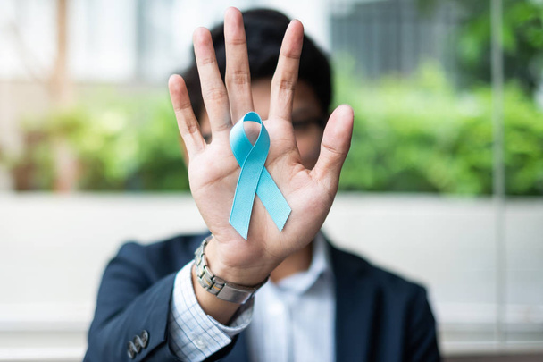 Ο μήνας ευαισθητοποίησης για τον καρκίνο του προστάτη, ο επιχειρηματικός άνθρωπος που κρατά ελαφρύ μπλε κορδέλα για τη στήριξη ανθρώπων που ζουν και ασθένειες. Ανδρική υγειονομική περίθαλψη και παγκόσμια έννοια της ημέρας του καρκίνου - Φωτογραφία, εικόνα