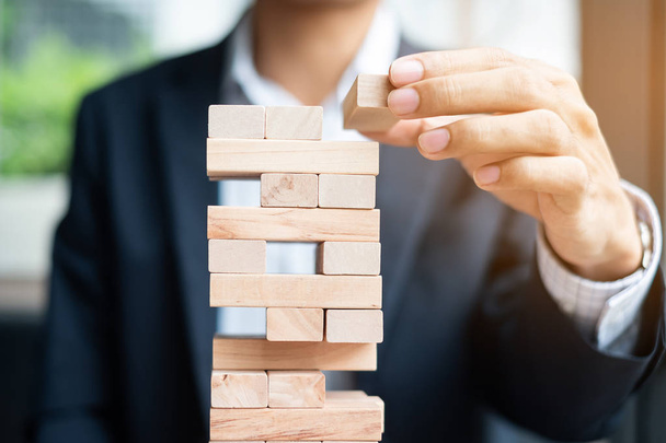 Businessman hand placing or pulling wooden block on the tower. Business planning, Risk Management, Solution and strategy Concepts - Photo, Image
