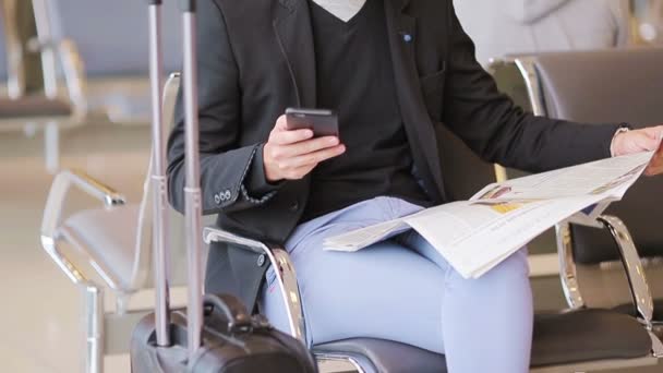Szekrény okostelefon férfi kezekben és újság belül a repülőtéren. Alkalmi üzletember öltönyben. Fiatal férfi mobiltelefonnal a reptéren, miközben a beszállásra vár.. - Felvétel, videó