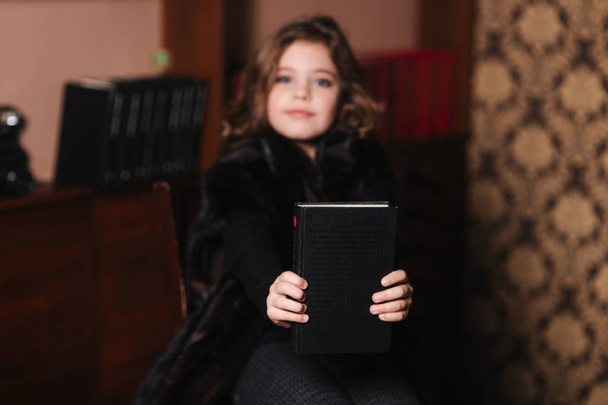 Beautiful little girl is reading a book in the library. Preparing for a school - Foto, afbeelding