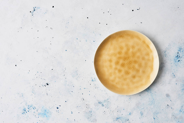 Modern pottery. Yellow dinner plate, Empty ceramic plate with abstract yellow texture on abstract white and blue stucco background. Top view with copy space. - Photo, Image