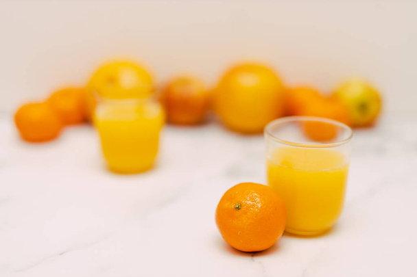 healthy fruit including oranges grapefruits and apples scattered on light-toned marble and with juice glasses, concept or eating vs drinking your vitamins - Foto, Imagem