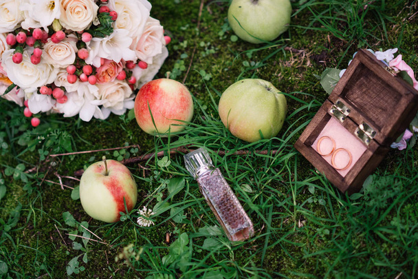 obrączki ślubne w drewnianym pudełku w trawie z jabłkami i perfum z Bukiet ślubny, kwiaty - Zdjęcie, obraz