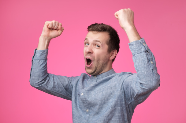 Happy young european man gesturing and smiling while standing against pink background - Фото, изображение