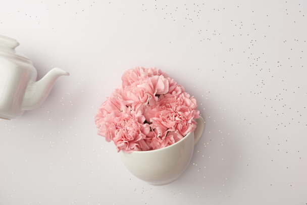 pink carnation flowers in cup and white kettle isolated on grey - Foto, imagen