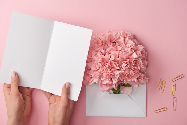 tartó üres kártya és a rózsaszín virágok borítékban elszigetelt rózsaszín női levágott lövés - Fotó, kép