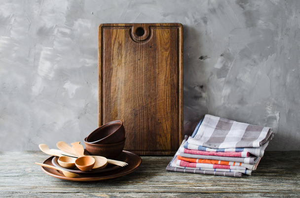 Simple rustic kitchenware: ceramic plates, wooden or bamboo cutlery, vintage cutting board and towels in interior of kitchen. Rustic style. Home Kitchen Decor. - Photo, image