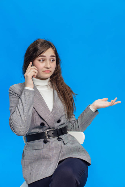 A beautiful girl on a blue background isolated holding a phone sits surprised - Photo, image