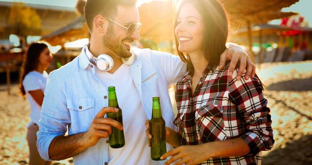 Happy young couple smiling and drinking beer at beach - Fotoğraf, Görsel