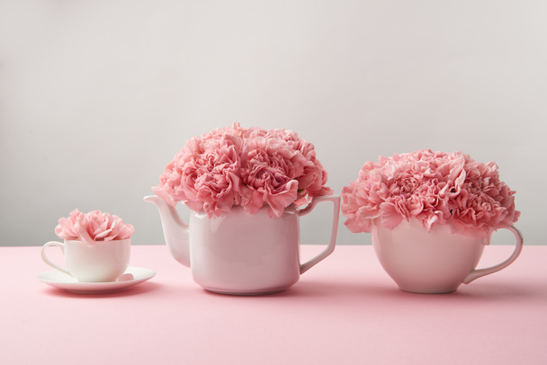 beautiful tender pink flowers in white teapot and cups on grey   - Photo, Image