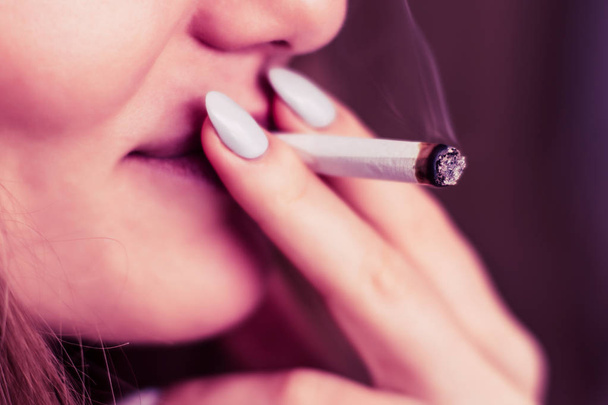 μια άρθρωση στο χέρι μια γυναίκα καπνίζει κάνναβη ζιζάνιο. Καπνού σε μαύρο φόντο. Έννοιες της ιατρική χρήση μαριχουάνα και τη νομιμοποίηση της κάνναβης. Σε ένα μαύρο φόντο ροζ χρωματισμό - Φωτογραφία, εικόνα