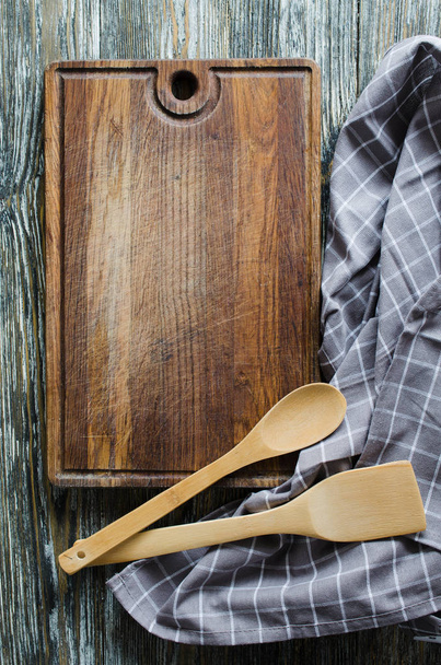 Culinary background with rustic kitchenware: wooden or bamboo cutlery, vintage cutting board and towel against vintage wooden background. Rustic style. Home Kitchen Decor. View from above. - 写真・画像