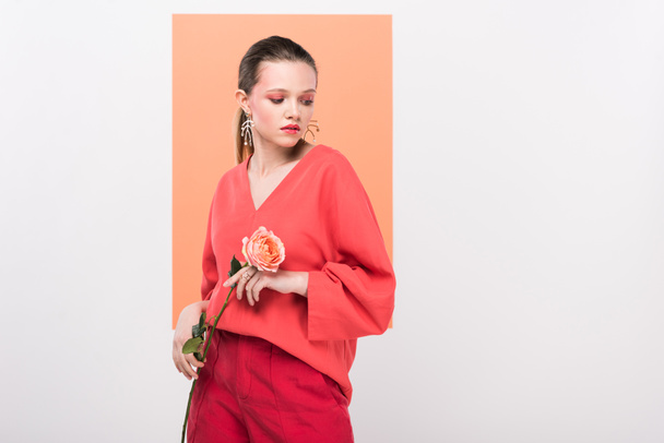 beautiful stylish girl holding rose, looking away and posing with living coral on background - Foto, imagen