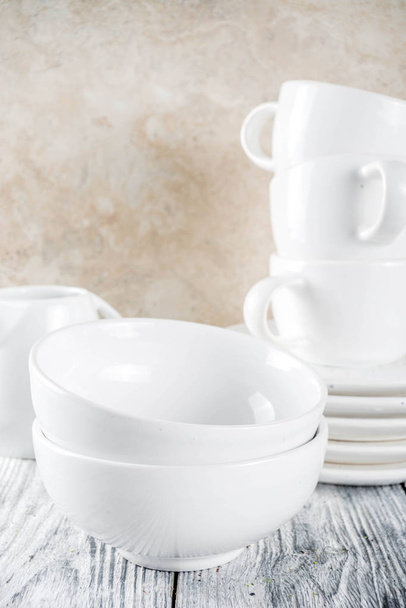 Ассортимент стек чистые пустые новые белые кухонные принадлежности, тарелки, миски, чашки кружки. На белом бетонном фоне
 - Фото, изображение