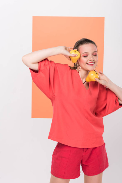 beautiful smiling fashionable girl holding pears and posing with living coral on background - Foto, afbeelding