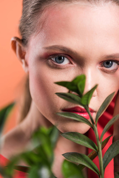 portrait of beautiful stylish girl looking at camera and posing with plant isolated on living coral - Foto, immagini