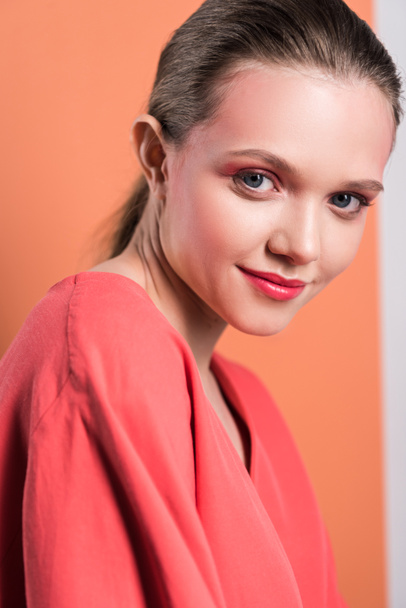 portrait of beautiful stylish girl looking at camera and smiling on living coral background - Foto, Imagem