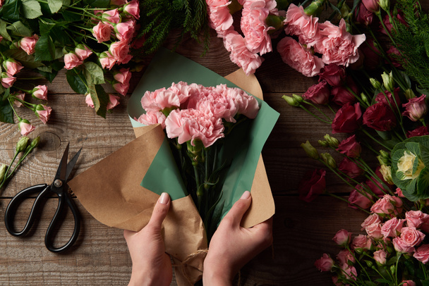 abgeschnittene Aufnahme einer Frau, die schöne Blumen in Bastelpapier in Holzoberfläche wickelt - Foto, Bild
