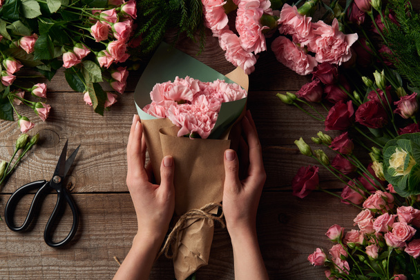 abgeschnittene Aufnahme weiblicher Hände mit schönem Strauß und zarten Blumen mit der Schere auf der Holzoberfläche  - Foto, Bild