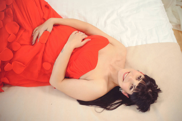 Novo conceito de vida. Gravidez, maternidade e felicidade. Close-up de mulher grávida em elegante vestido vermelho elegante na vista superior da cama - Imagem
 - Foto, Imagem