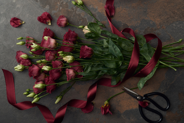 Draufsicht auf wunderschöne Eustoma-Blumen mit Schleife und Schere auf dunkler Oberfläche    - Foto, Bild