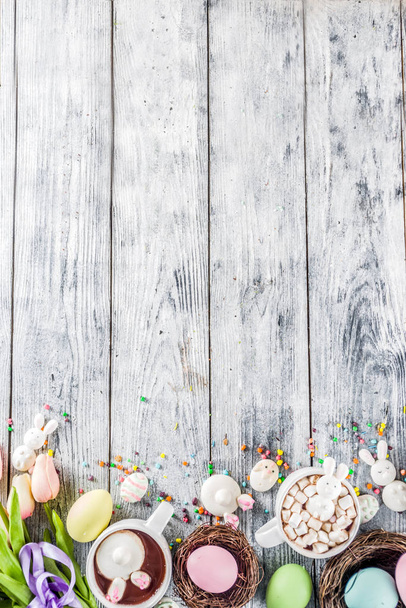 Easter funny kids food and drink concept, sweet hot chocolate with marshmallow bunny rabbits and easter eggs, wooden background copy space top view - 写真・画像