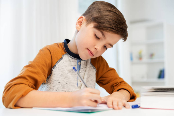 boy doing homework and writing to notebook at home - Foto, imagen