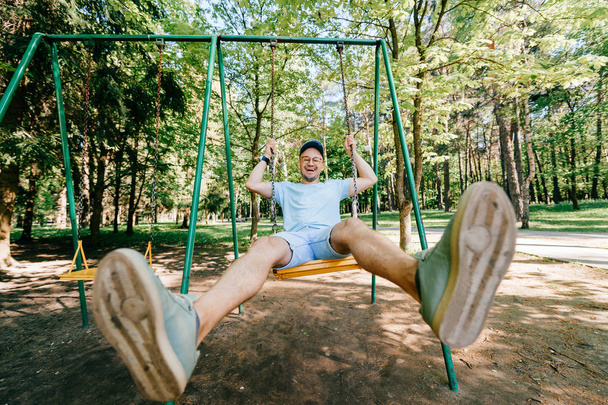 Aikuinen mies keinuvat keinu leikkikentällä kesäpuistossa
 - Valokuva, kuva