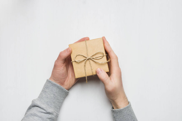 man's hands holds a gift in a box on a white wooden background - Foto, imagen