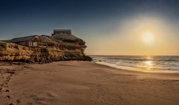 Beautiful sunset with cliff and wooden houses along the coast line of Namibe beach. Africa. Angola. - Photo, Image
