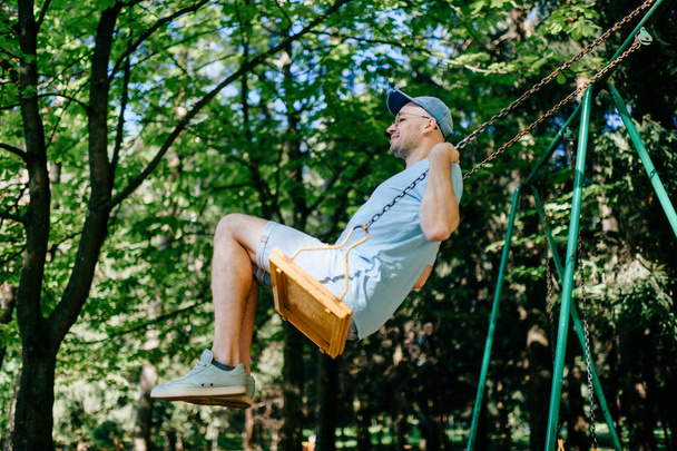 adult man swinging on swing on playground in summer park - Foto, Imagem