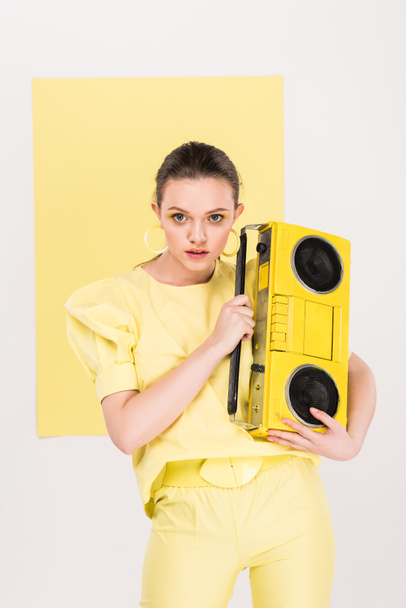 stylish girl holding retro boombox, looking at camera and posing with limelight on background - Photo, Image