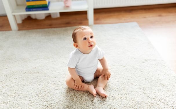bebé sentado en el suelo en casa y mirando hacia arriba
 - Foto, Imagen