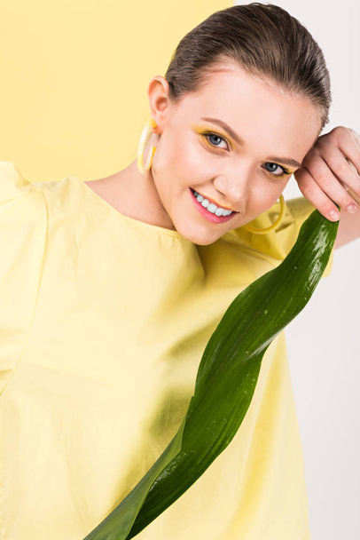 beautiful stylish girl holding leaf, looking at camera and posing with limelight on background - Photo, Image