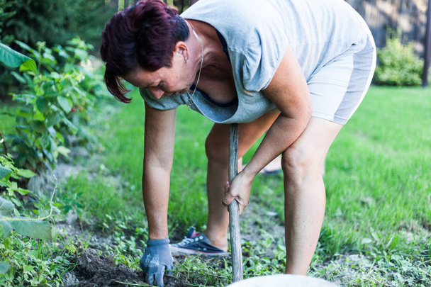 A brunet woman working hard on the vegetable garden. The gardener busy cultivating the topsoil. Preparing the backyard for planting crops. Organic farming concept. - Photo, Image