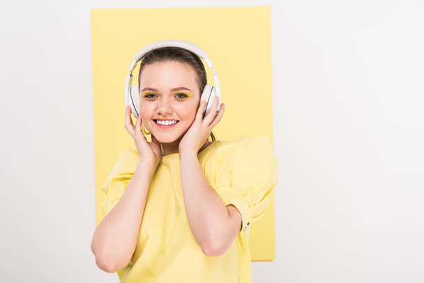 beautiful stylish girl in headphones looking at camera and listening music with limelight on background - Fotografie, Obrázek