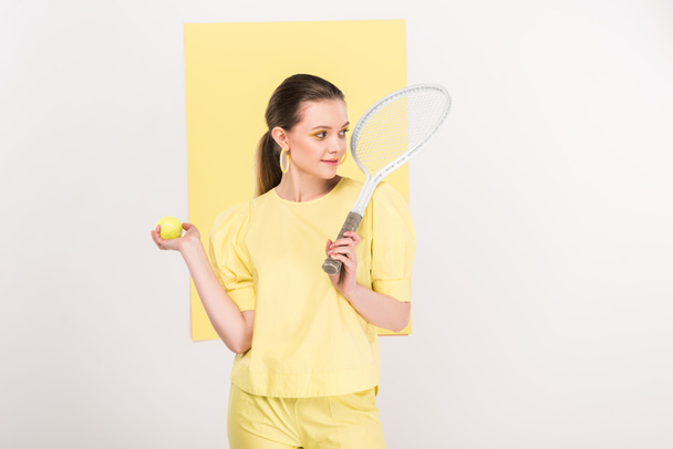 hermosa chica elegante sosteniendo raqueta de tenis y pelota mientras posa con centro de atención en el fondo
 - Foto, imagen