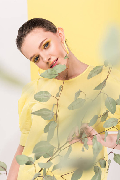 selective focus of attractive stylish girl holding plant and posing with limelight on background - Foto, imagen