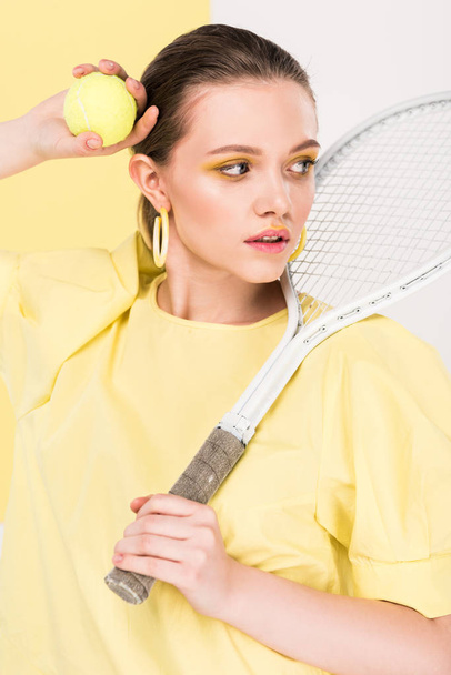 beautiful stylish girl holding tennis racket and ball while posing with limelight on background - Fotografie, Obrázek