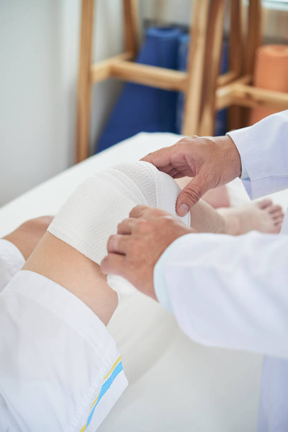 Shůry záběr plodin praktického lékaře použití čisté bandáž na koleno k nepoznání pacienta  - Fotografie, Obrázek